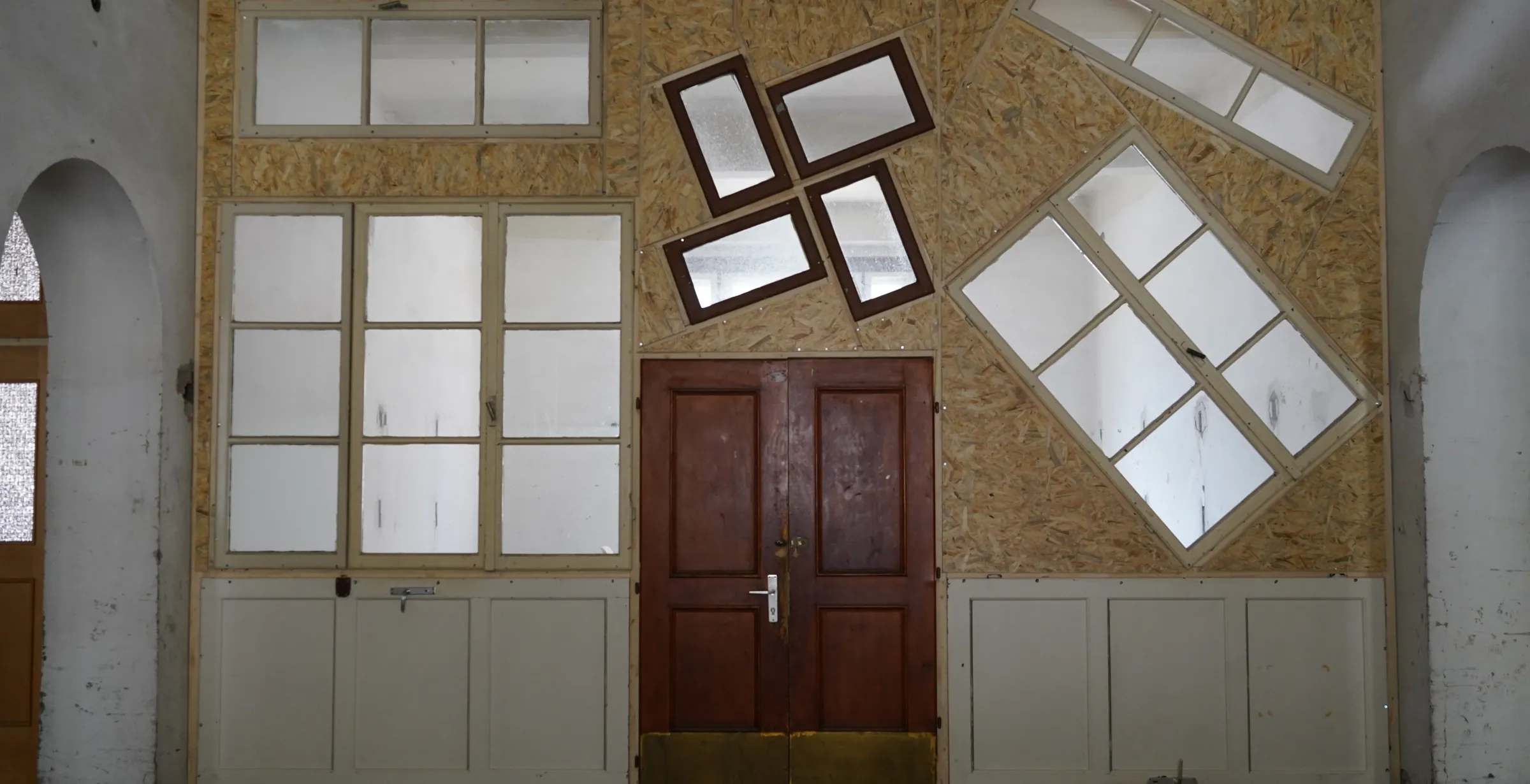Ausgebaute alte Fenster und eine Holztür, an einer Wand aufgereiht